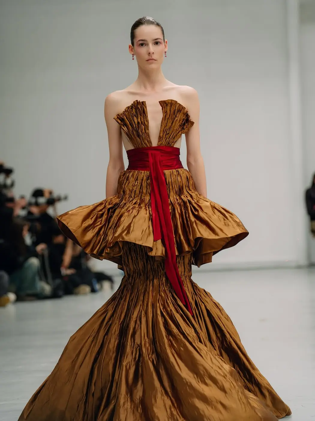 A model in a bronze ruffled gown with a red sash