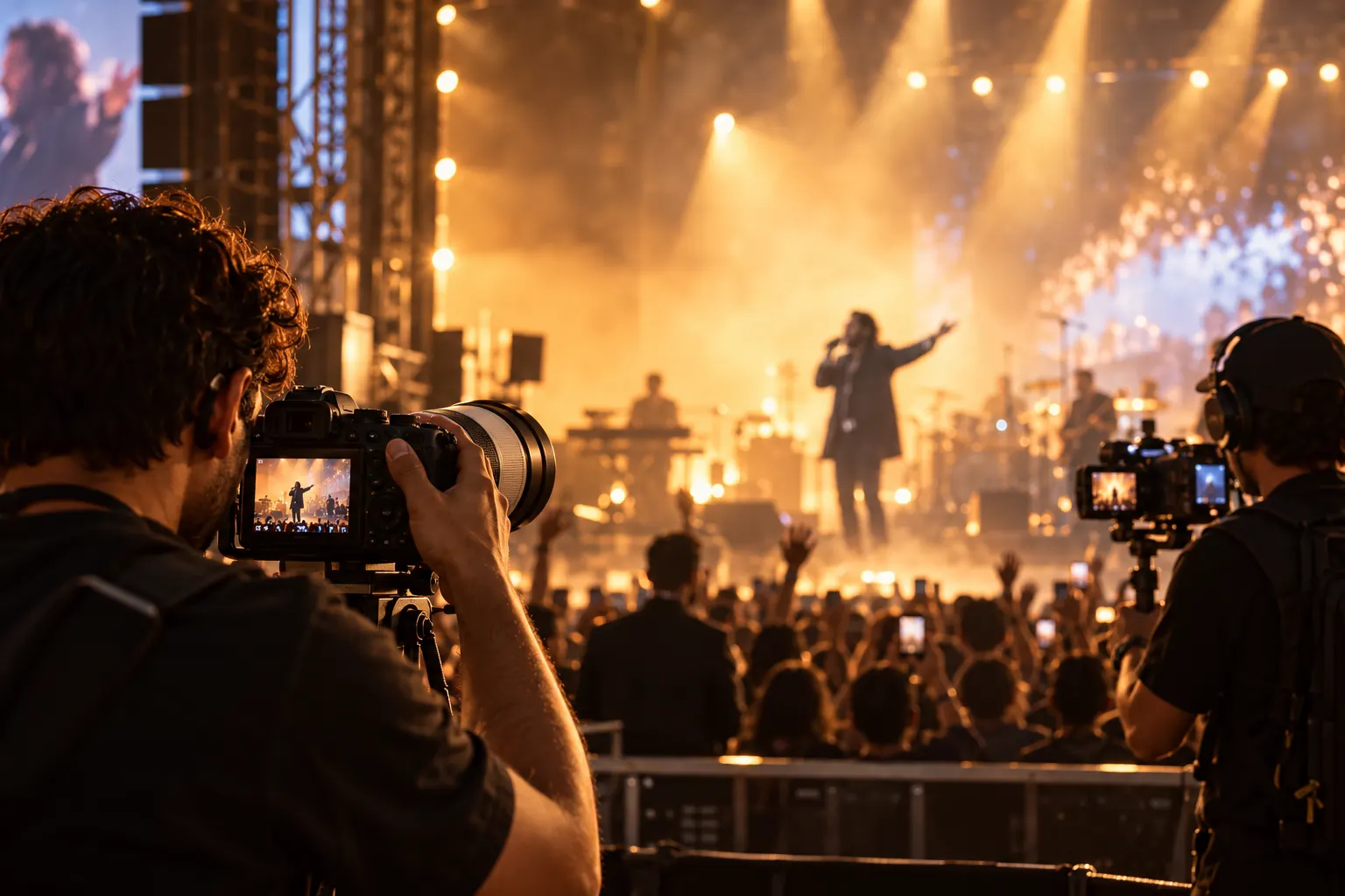 A photographer and videographer capturing a performer on a golden-lit concert stage